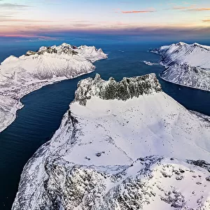 Romantic sunrise over the snowy peak of Grytetippen mountain along the icy sea, aerial view, Ornfjord, Senja, Troms, Norway