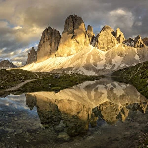 Tre Cime di Lavaredo are reflected in an alpine lake during a sunset with warm light