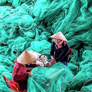 Vietnam, Cam Ranh, two men repair green fishing nets using a sewing machine