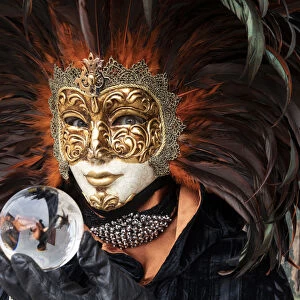 A woman in a feather Venetian mask poses with a glass ball during the Venice Carnival