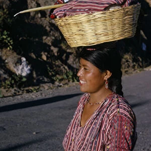 GUATEMALA, Lake Atitlan Indian girl walking along road carrying a basket of washing