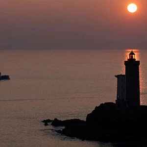 A boat makes his way behind the Phare du Petit Minou as the sun sets over the Atlantic
