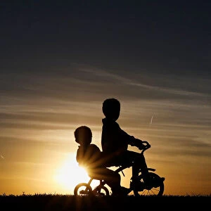 Children are seen in silhouette riding a tricycle along the Mississippi River Park at