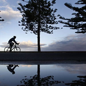 A cyclist is seen reflected while riding along a beach in Melbourne