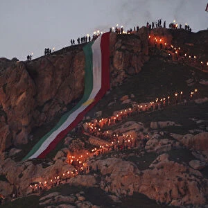 Iraqi Kurdish people carry fire torches up a mountain where a giant flag of Iraq s