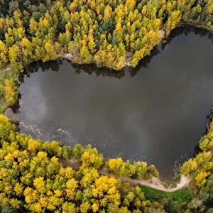 A lake in a shape of a heart is seen surrounded by autumn-coloured trees outside