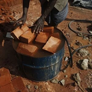 A man puts bricks into an oil barrel which filled with water at a construction site in