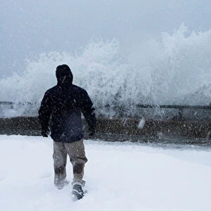 A man watches as ocean waves overtop the seawall during a winter snow storm in the Boston