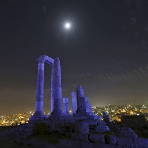 The moon is seen over the Roman pillars of the Temple of Hercules as it is lit up in blue