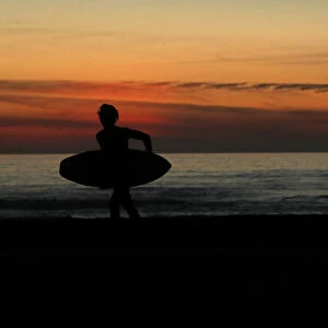 A surfer carries his board off the beach after surfing in Cardiff, California