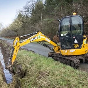 Cleaning out roadside drainage ditches which had become overgrown using JCB digger, England, February