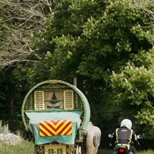 Motorcyclist overtaking horse drawn traveller caravan on rural road, Cumbria, England, June