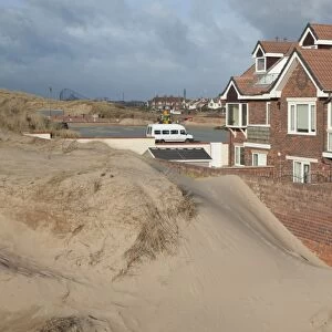 Sand blown from beach forming dunes building up against garden wall next to houses in seaside resort town, Lytham St. Anne's, Lancashire, England, january