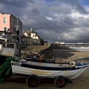 View of fishing boats, beach and pier of seaside town, with stormclouds overhead, Cromer Pier, Cromer, Norfolk