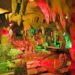 A cave of stalagmites and stalactites lighted with colored lights near the entrance