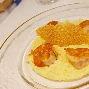 A creamy risotto with confit lemon and thyme grilled scampis on a glass plate with