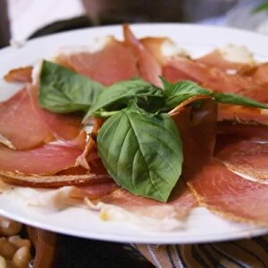 Dried dry cured ham with basil leaves on a white plate. Tradita traditional restaurant, Shkodra
