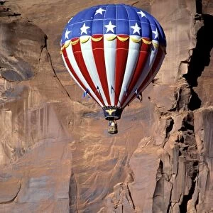 USA, Utah, Monument Valley. A patriotic hot-air balloon floats by a red rock wall