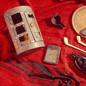 Articles carried by soldiers at the time of the American Revolutionary War. From upper left are: tin lantern; wrought iron open lamp; wooden plate or trencher; forged iron tablespoon; white clay pipes; medicine bottle; mirror