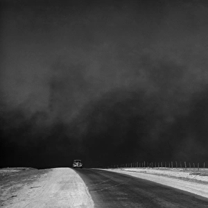 DUST BOWL, 1936. A car on a deserted road with black clouds of dust rising from the horizon, Texas Panhandle, Texas. Photograph by Arthur Rothstein in March 1936