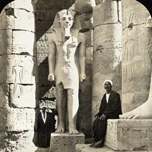EGYPT: LUXOR TEMPLE. A man seated next to a statue of Ramesses II at the Luxor Temple