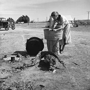 MIGRANT CAMP, 1937. A woman washing clothes in a washbin at a camp for migrant