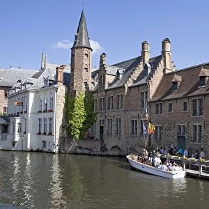 Belgium, West Flanders, Bruges, view of canal and tourists queuing up next to a tourboat