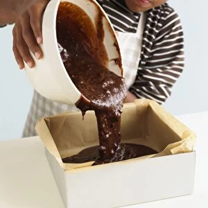 Boy pouring chocolate brownie cake mixture into tin lined with wax paper, close-up