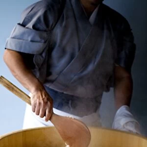 Chef stirring rice in wooden barrel, using wooden spoon, close-up