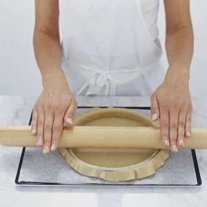 Chef using rolling pin to remove excess pastry from cake tin