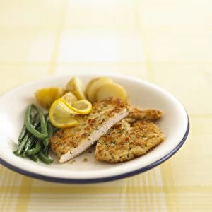 Chicken escalope coated with bread crumbs, served with French beans and boiled potatoes, garnished with sliced lemons and parsley