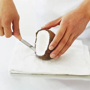 Coconut flesh being cut away from shell with a knife, high angle view