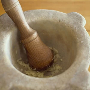 Crushed garlic in stone mortar bowl with wooden pestle, close-up, high angle view