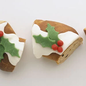 Three festive pieces of fruity bread topped with white icing and holly icing, green leaves and red berries made of marzipan, above view