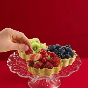 Hand removing raspberry from tartlet on cut glass cakestand