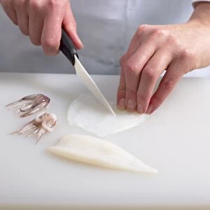 Hands holding knife cutting squid into strips, tentacles nearby, close-up