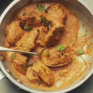 Large pan with prawns, red peppers, green herbs and red sauce Chicken tikka masala garnished with coriander leaves being spooned out of a pan, view from above