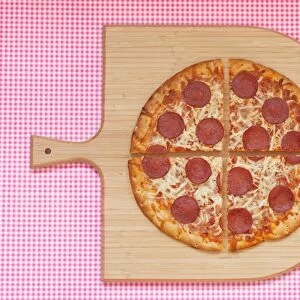 Pepperoni pizza cut into four quarters on a chopping board, against a checked background