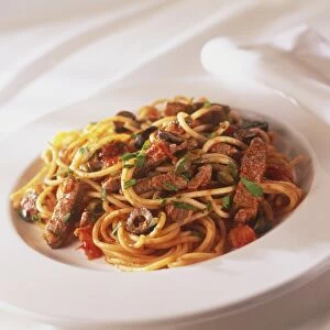 Plate of spaghetti pizzailola with strips of fried red meat, sprinkled with fresh herbs, close up