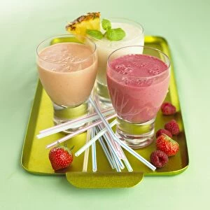 Smoothies, drinking straws and fresh fruit on a gold tray