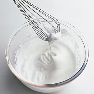 Whisk and whisked egg whites in glass mixing bowl, close-up