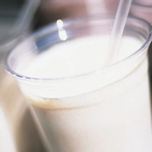White creamy milkshake in plastic cup with straw, close-up