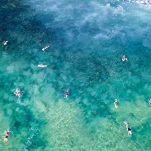 Aerial View over blue and green clear ocean waters with surfers