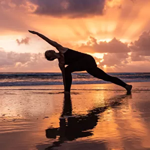Woman doing Yoga on the beach at sunrise