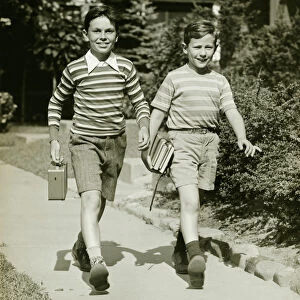 Two boys (10-11) walking side by side in suburbs, carrying books, (B&W)