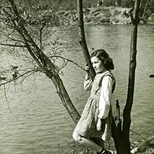 Girl (8-9) leaning on tree trunk by water, (B&W), elevated view