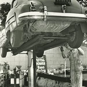 Man repairing uplifted car, (B&W), low section