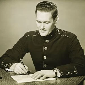 Marine in military uniform writing letter at desk, (B&W)