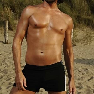 Muscular man wearing swimming trunks posing on beach