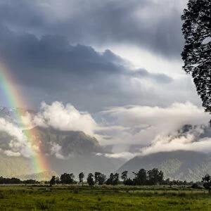 Storm clouds with rainbow, pasture against the Southern Alps, Fox, South Island, New Zealand
